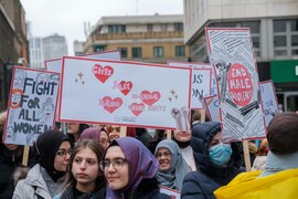 Women wearing headscarves holding signs that read "Fight for All Women," "Girls Just Wanna Have Equal Rights," and "End Male Violence."