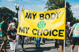 A group of people walking down a street holding a yellow sign that reads "My Body My Choice."
