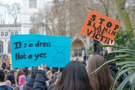 Women marching in the 97% March in the UK, holding signs that read "It's a Dress, Not a Yes," and "Stop Blaming the Victim."