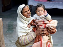 An older woman wearing a headscarf holds a baby who is waving.