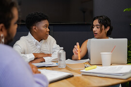 A trans person and a trans man discussing something in a meeting.