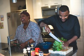 A Black man and woman prepare vegetables at a kitchen island.