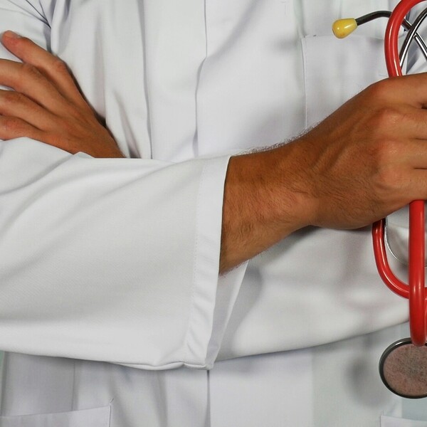 Torso of doctor in white coat with arms crossed and red stethoscope around neck.