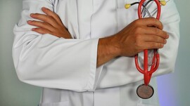 Torso of doctor in white coat with arms crossed and red stethoscope around neck.