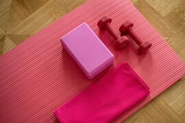 Pink exercise mat with pink dumbbells, pink yoga block, and pink towel.