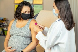 A pregnant woman wearing a face mask is being examined by a doctor.