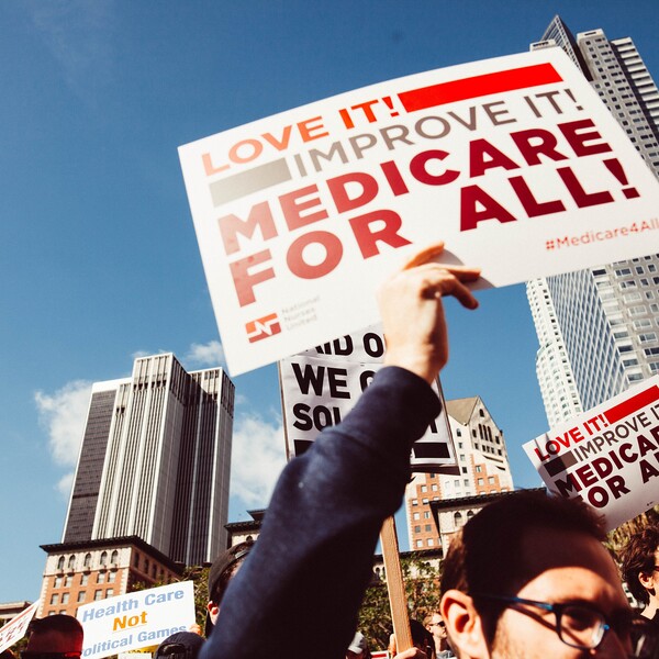 People at a Medicare for All rally holding signs that say "Love It! Improve It! Medicare for All."