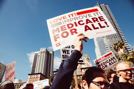 People at a Medicare for All rally holding signs that say "Love It! Improve It! Medicare for All."