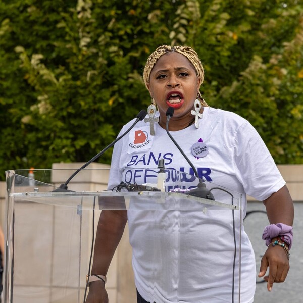 A Black woman wearing a shirt that reads "Bans Off Our Bodies" speaks at a podium.