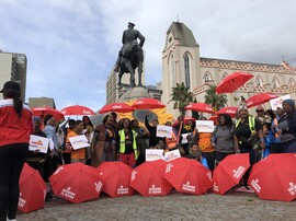 A large gathering of people with posters and red umbrellas that read "Sex Work is Work."