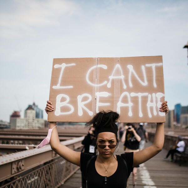A Black woman holds a sign above her head which reads "I can't breathe."