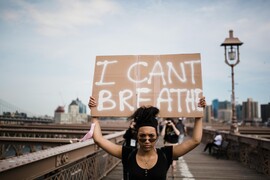 A Black woman holds a sign above her head which reads "I can't breathe."