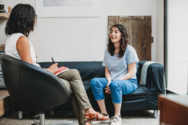 Woman sitting in chair talking to seated psychologist in office.