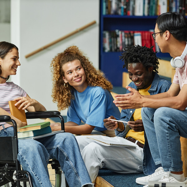 Diverse group of young people chatting in college library including female student in wheelchair.