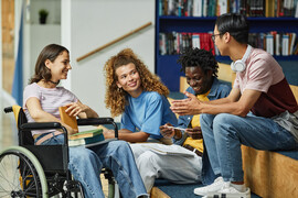 Diverse group of young people chatting in college library including female student in wheelchair.