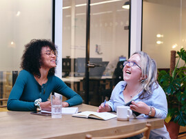 Two smiling women writing in notebooks in modern office.