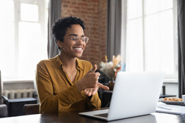 Smiling Black woman in glasses is using sign language to talk on a video call.