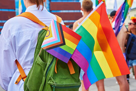 Intersex-inclusive progress pride flag and rainbow pride flag sticking out of a green backpack.