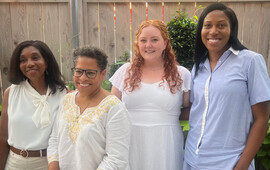 Four smiling women wearing white, posing outdoors