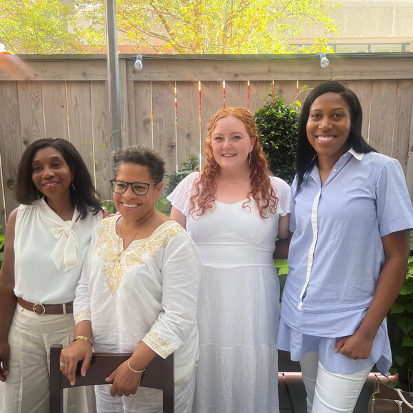 Four smiling women wearing white, posing outdoors